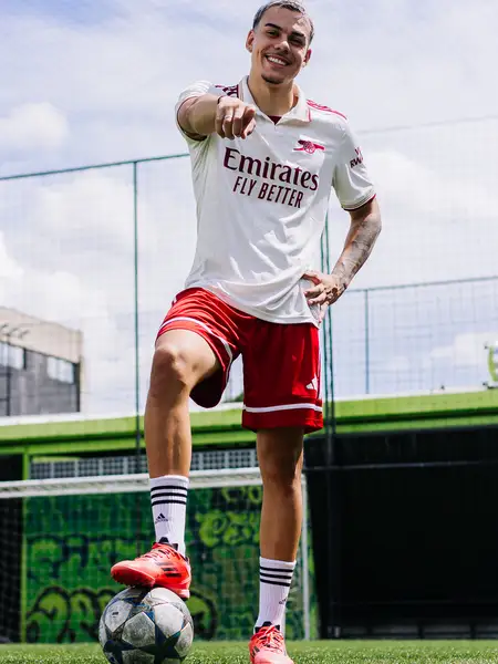Dudu Footz pointing at the camera with his foot on a football, on a pitch