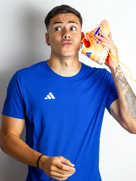 Dudu Footz holding a football boot to his ear like he's listening to something funny
