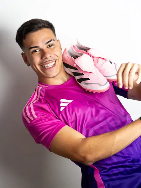 Dudu Footz smiling with a pair of pink football boots over his shoulder